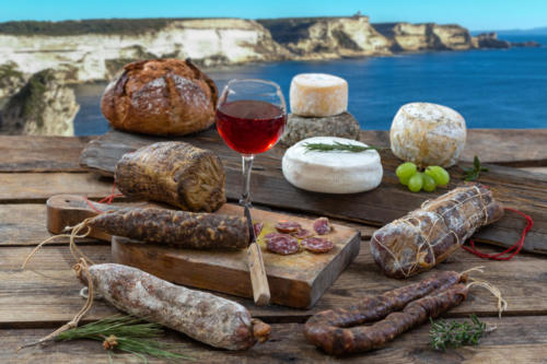 Corsican specialities: delicatessen, and cheese made in Corsica with the Porto veccio bay cliff panorama background, with a glass of wine